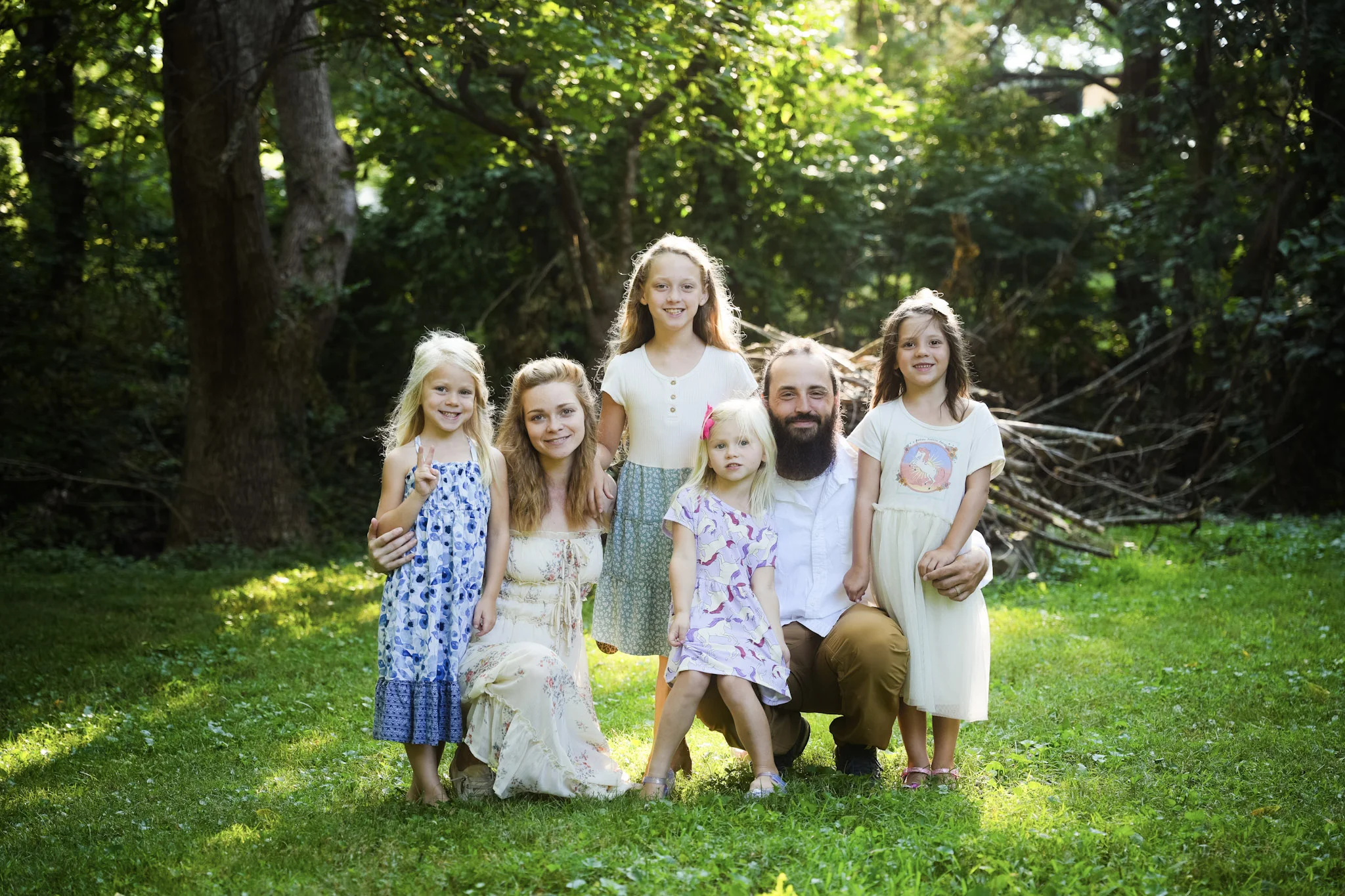 Family of six posing together in a sunlit park with trees in the background